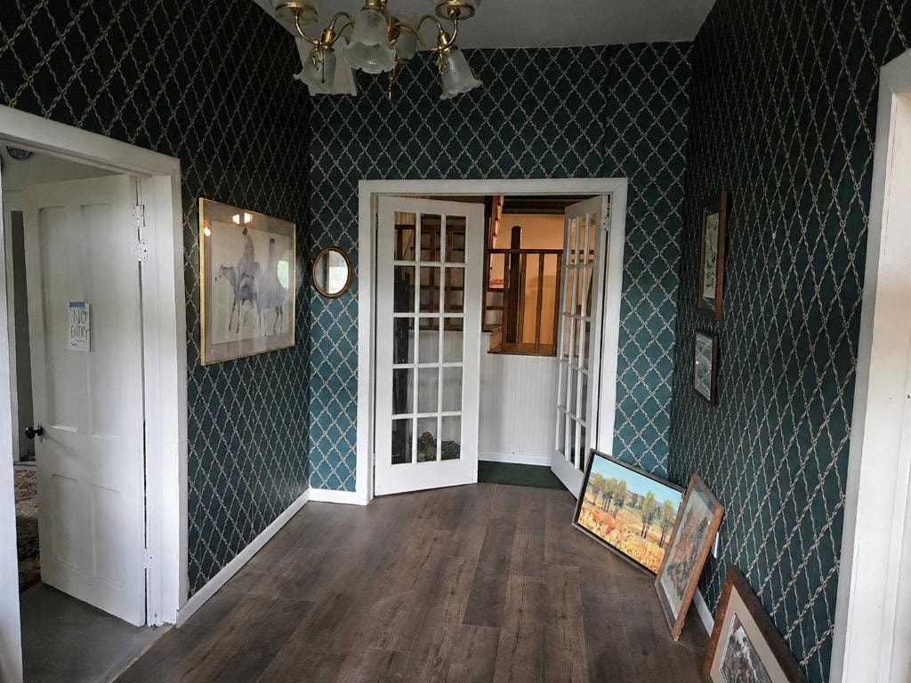Original foyer with teal patterned wallpaper, French doors, brass chandelier, and hardwood floors at 19 Talonah prior to renovation